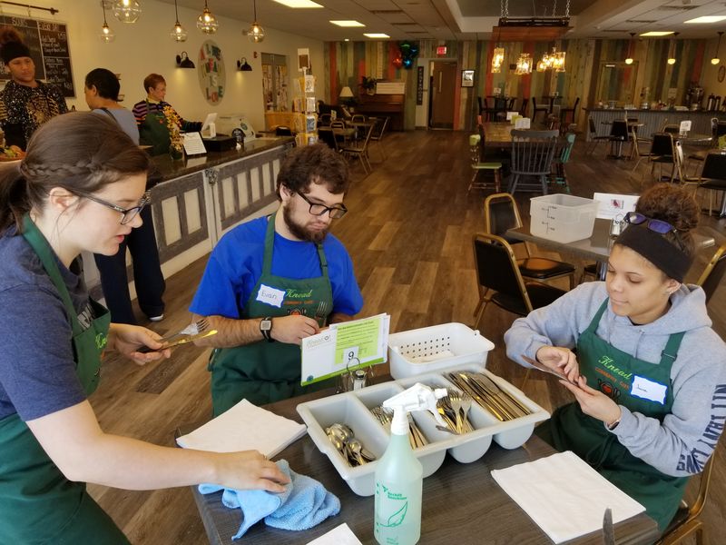 Student volunteers organize silverware at a table at Knead Cafe