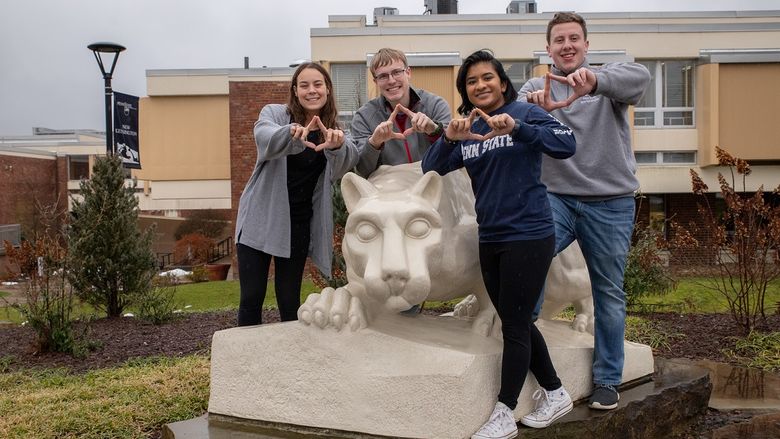 Four students stand by lion statue