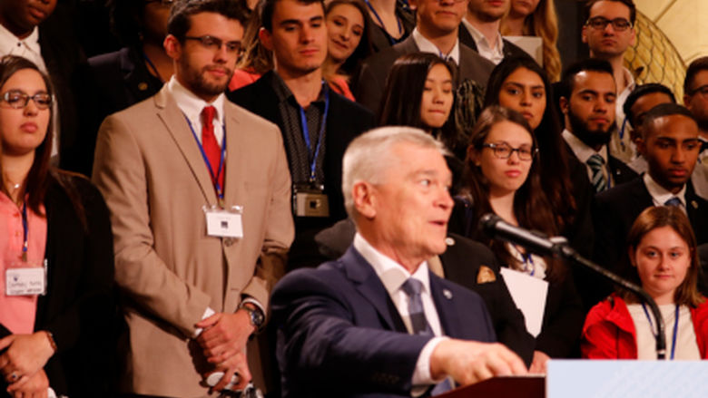 man speaking into microphone with students standing behind him