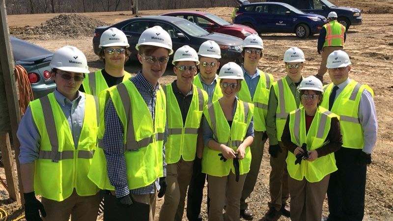 GREAT Program students and staff wear bright yellow vests and white hard hats while visiting a Massaro construction site