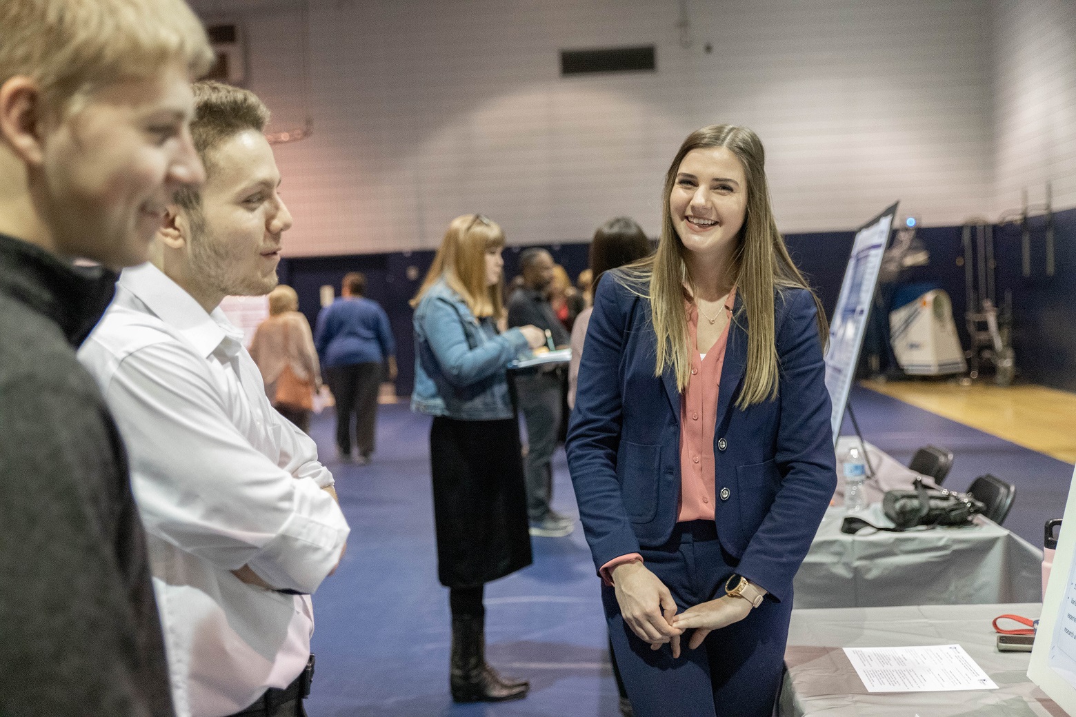 Female student smiles as two male students look at research poster