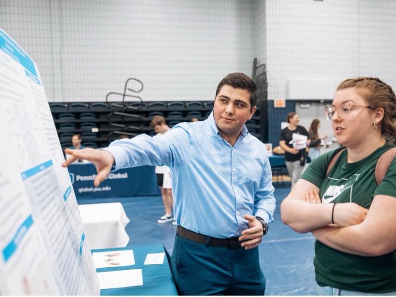 A student points to his research poster board, explaining its contents to an interested visitor.