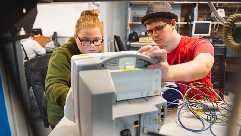 Two students work on hospital equipment in lab