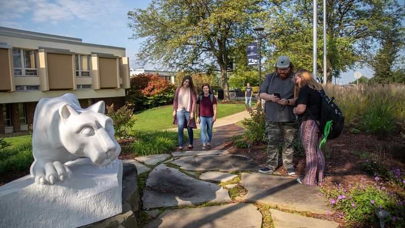 Students standing and walking by lion statue