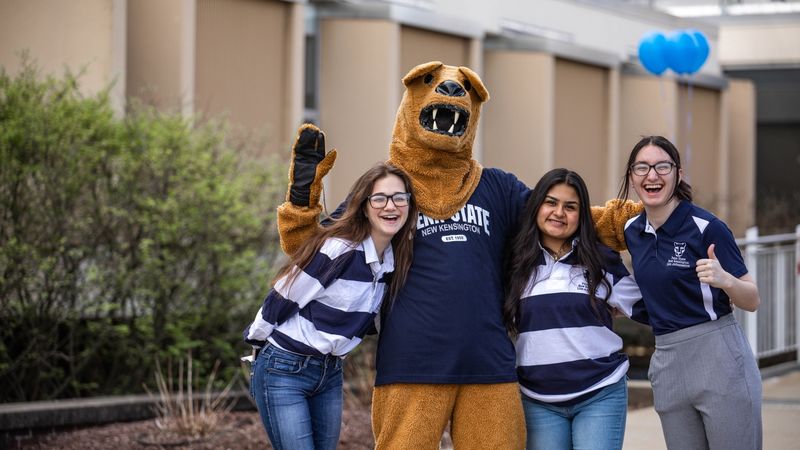 Three students and mascot pose for photo