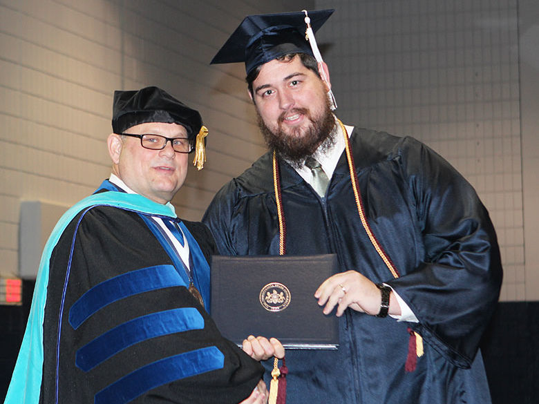 A new graduate receives his diploma from the Chancellor during a commencement ceremony