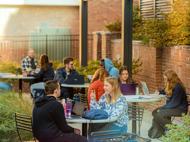 Campus courtyard with students seated around tables and taking in some sun