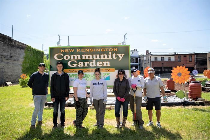 Seven men and women stand in community garden