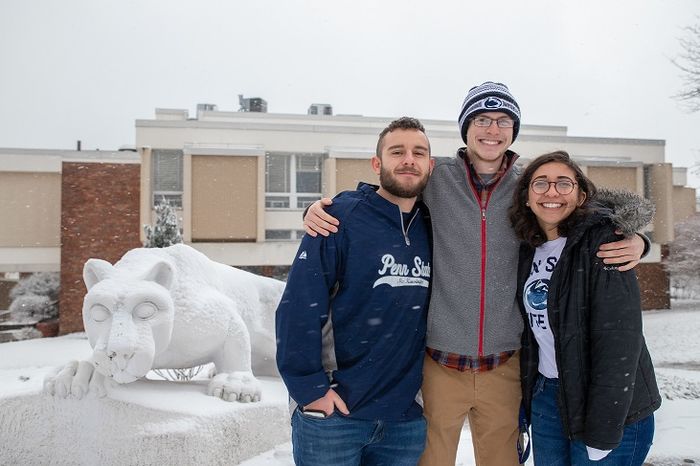 Three students stand next to Nittany Lion statue