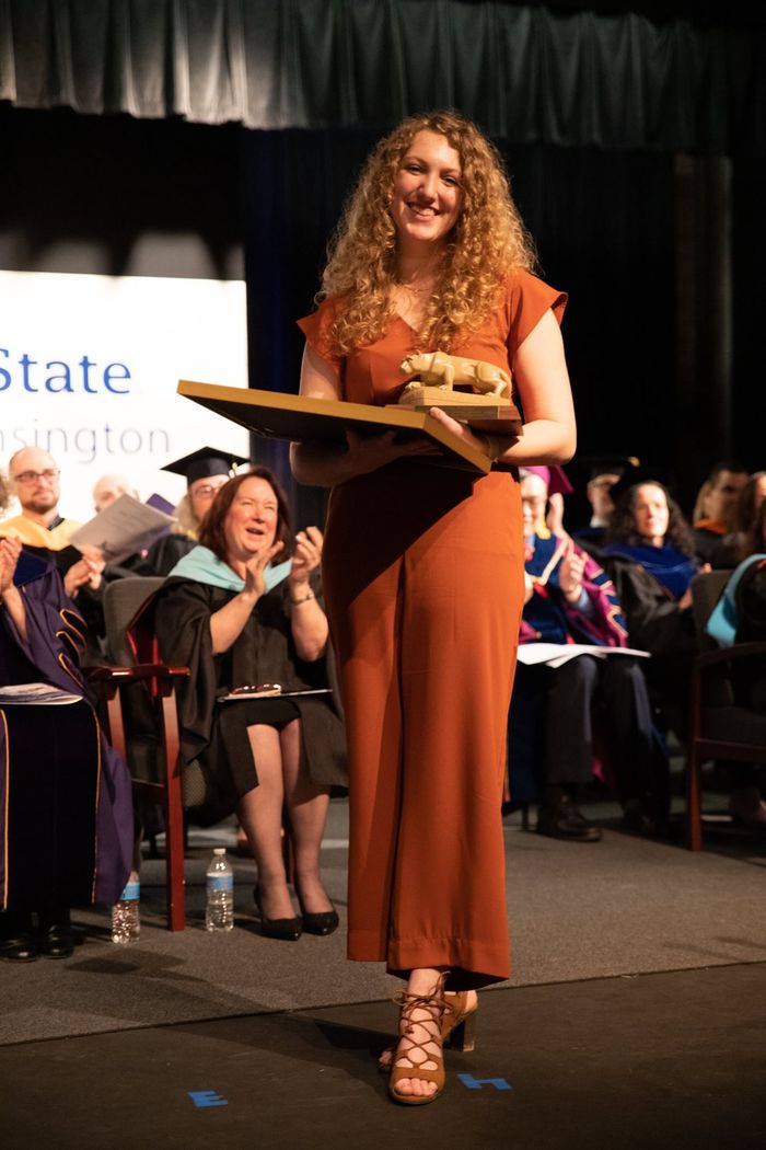 Female student stands on stage holding award