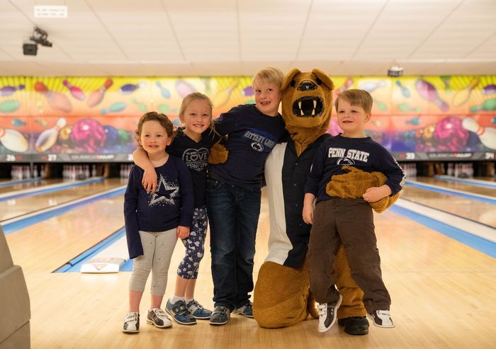 Two young boys and girls stand with Nittany Lion mascot at bowling alley