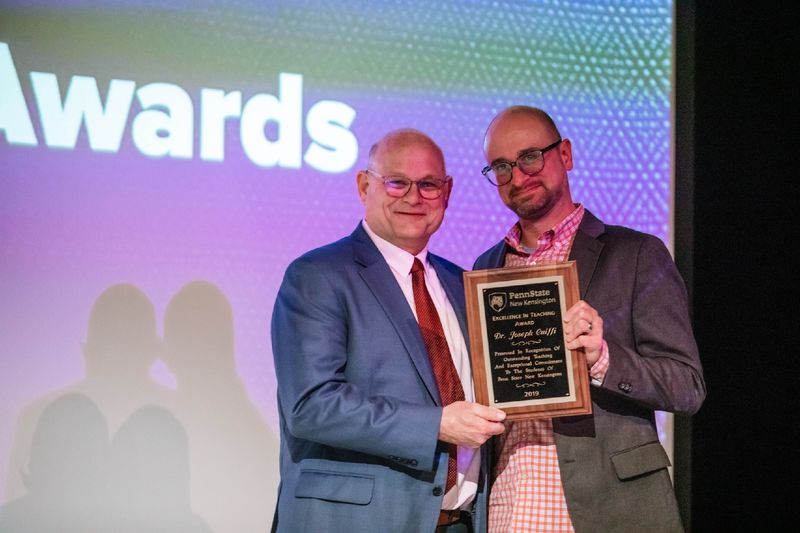 Two people stand holding a plaque