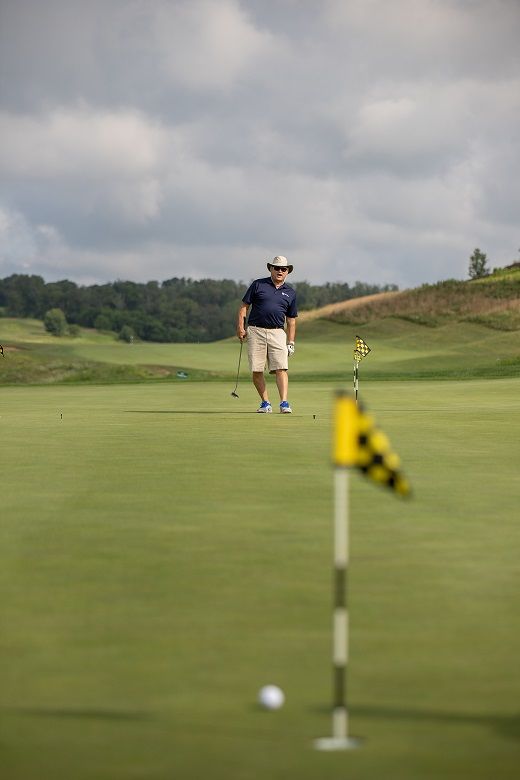 Man watches golf ball on green after putt Man watches golf ball on green after putt