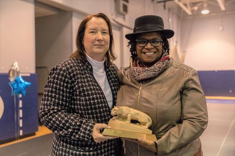 Two women stand holding a Nittany Lion statuette