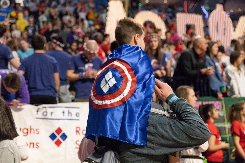 Child wearing cape sits on man's shoulder