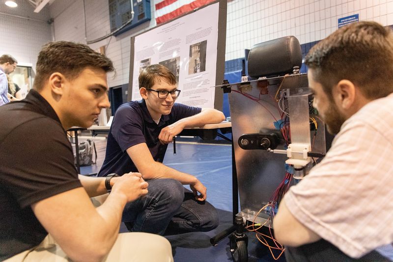 Three male students look at autonomous wheelchair