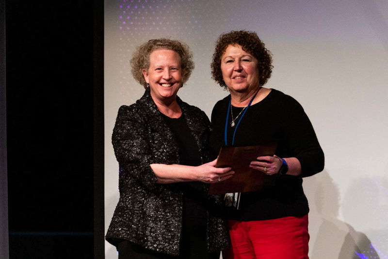 Faculty member holds plaque and stands next to Director of Academic Affairs