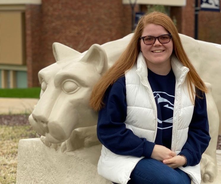 Female student sits next to lion shrine statue