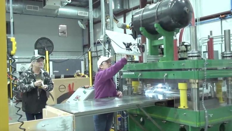 Two people in baseball caps and safety glasses work in a manufacturing plant 