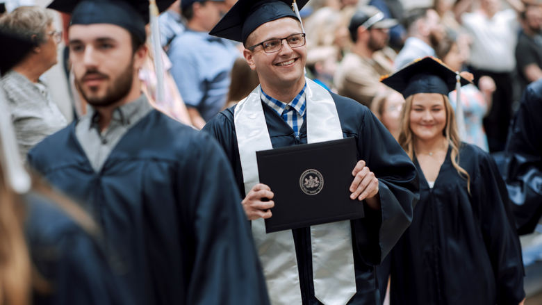 New Penn State graduate Kolton Lyons, who earned an associate degree in business administration, proudly displays his degree to onlooking family and friends during the commencement ceremony at Penn State DuBois.