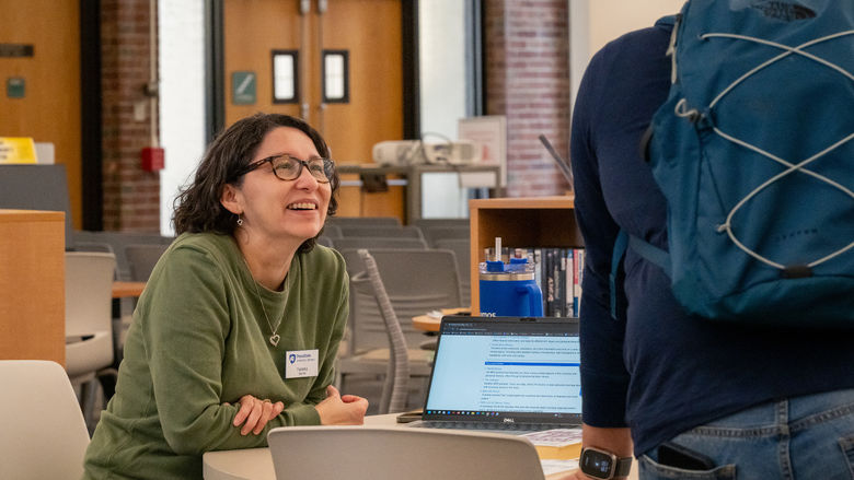 Yesenia, Library Operations Supervisor at Penn State New Kensington's Blissell Library, chats with a student near an information desk.