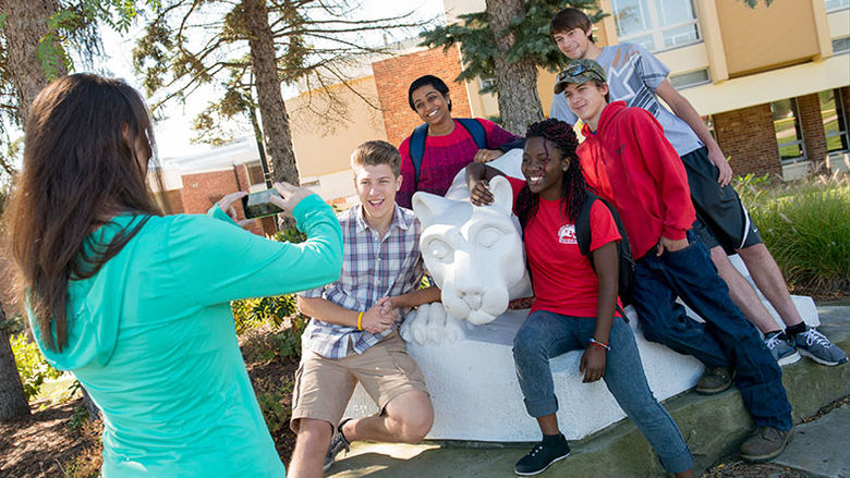Five individuals pose for a photo by the campus lion shrine