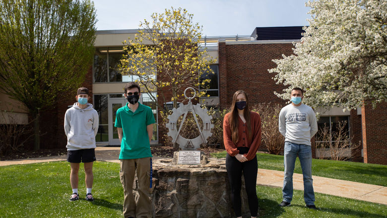 Four students stand outside by statue