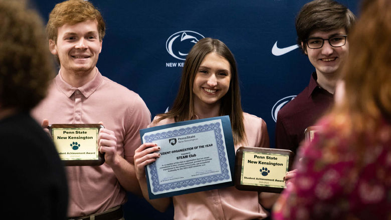 Three students smile to take photo while holding awards
