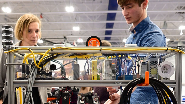 Dr. Megan Nagel, regional chancellor, listens as a student explains his engineering project at Penn State New Kensington’s annual Research and Student Engagement Expo. Cables and equipment are visible in the foreground as part of the student’s display.