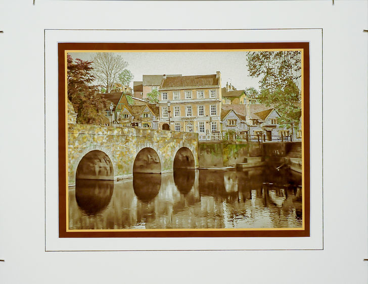 Hand-colored, monochrome photograph of stone bridge and building by Frank Santimauro