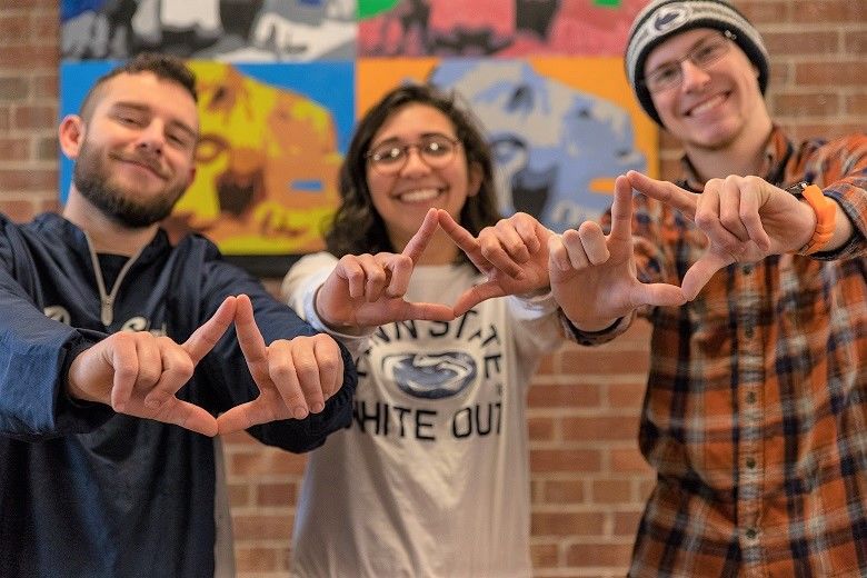 Three students stand with hands shaped like diamonds for THON