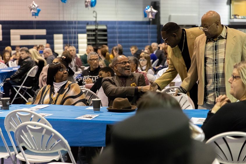 Men shake hands among guests sitting at table