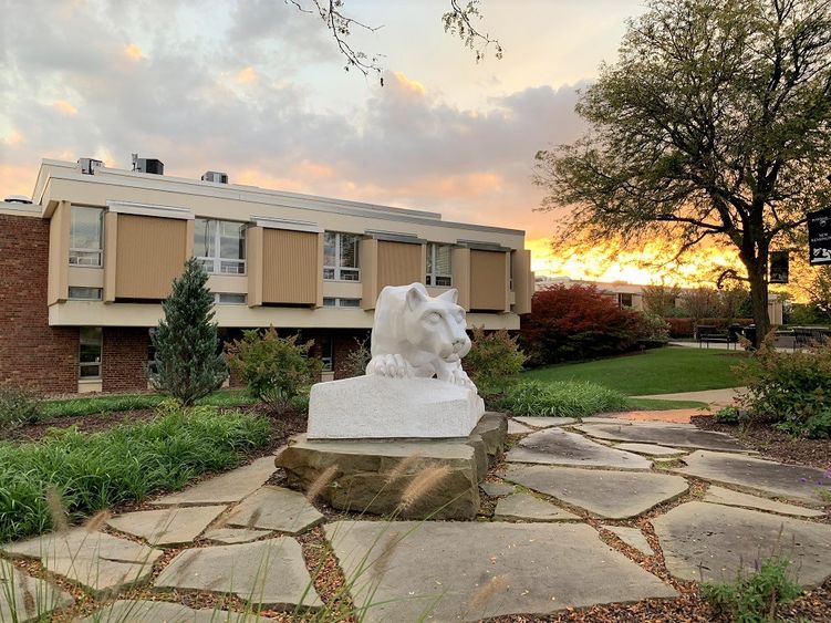 Nittany lion statue in foreground with campus buildings in background