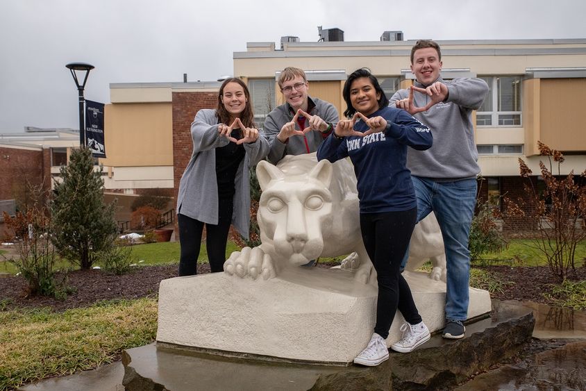 Four students stand by lion statue