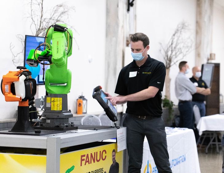 Man wearing mask holds digital tablet in front of robotic arm