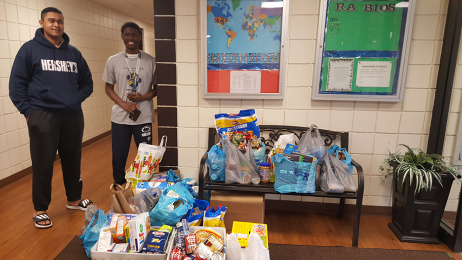 Two students stand by donated food and paper products
