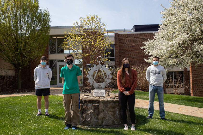 Four students stand outside by statue