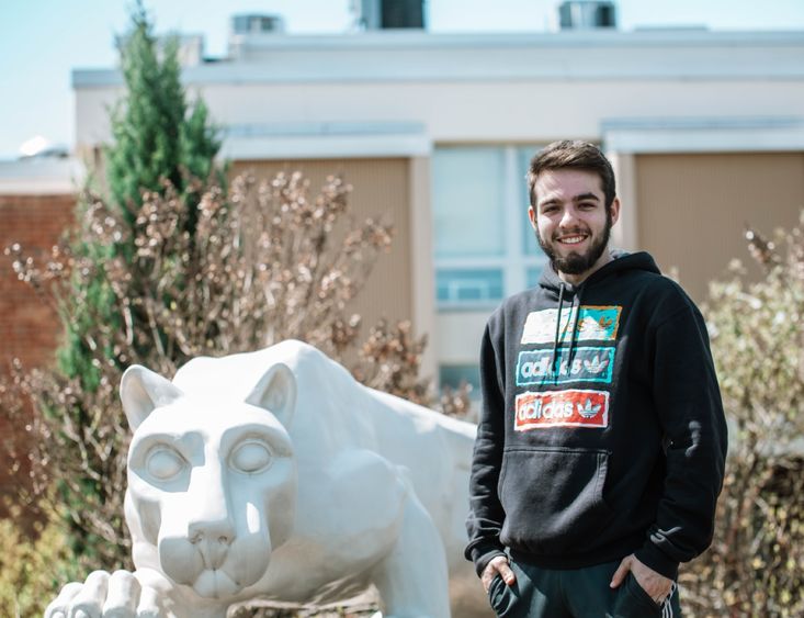 Student stands next to lion statue