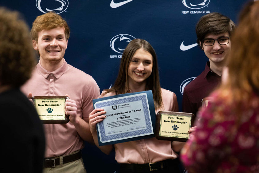Three students smile to take photo while holding awards